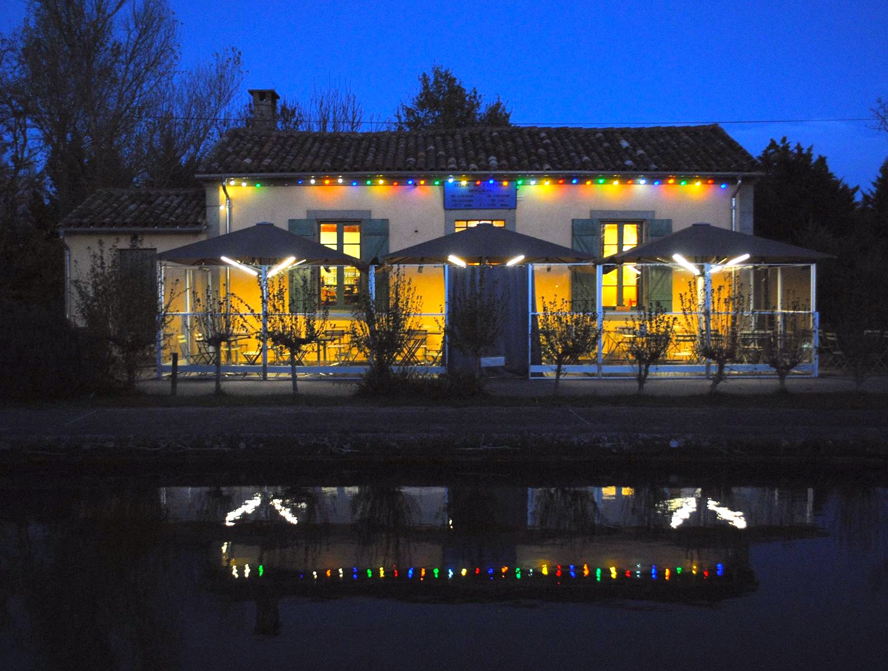 La maison éclusière de L'Écluse illuminée la nuit, reflétée dans le Canal du Midi